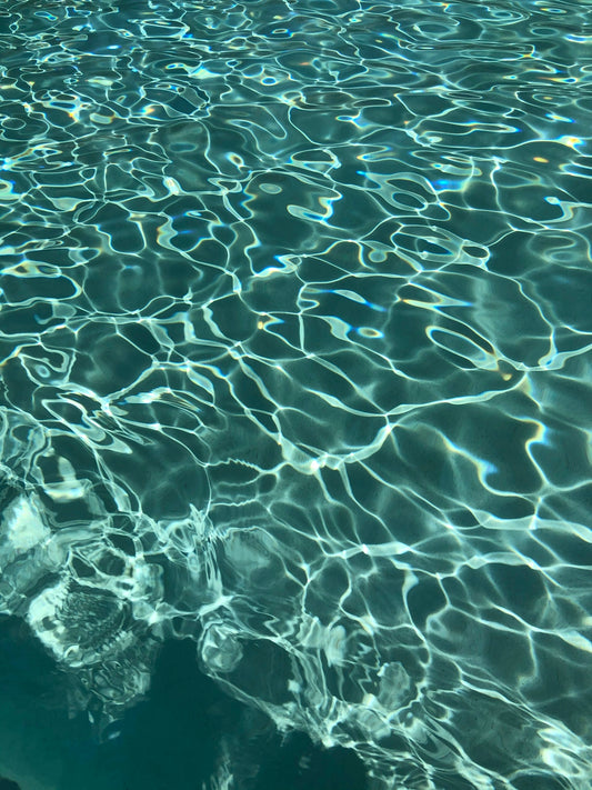 Sunlight reflecting on the rippling surface of clear blue swimming pool water