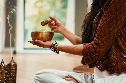 A person holding a singing bowl and striker with incense smoke in a room