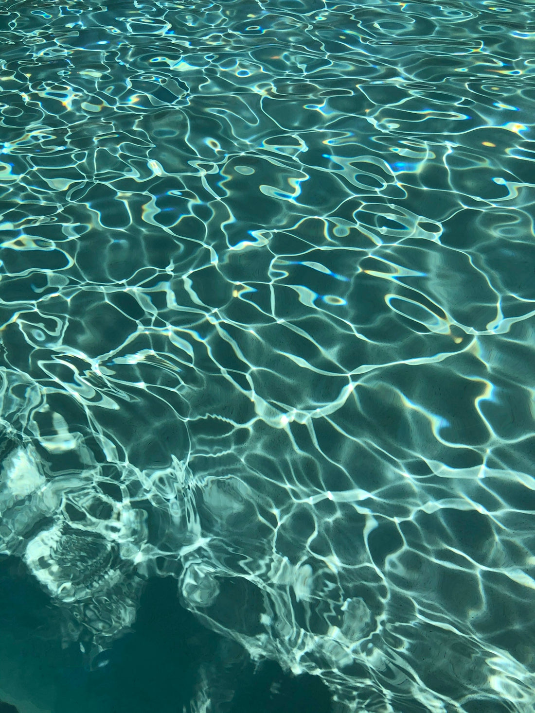 Sunlight reflecting on the rippling surface of clear blue swimming pool water