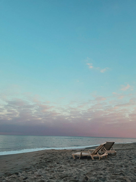 a couple of lawn chairs sitting on top of a sandy beach
