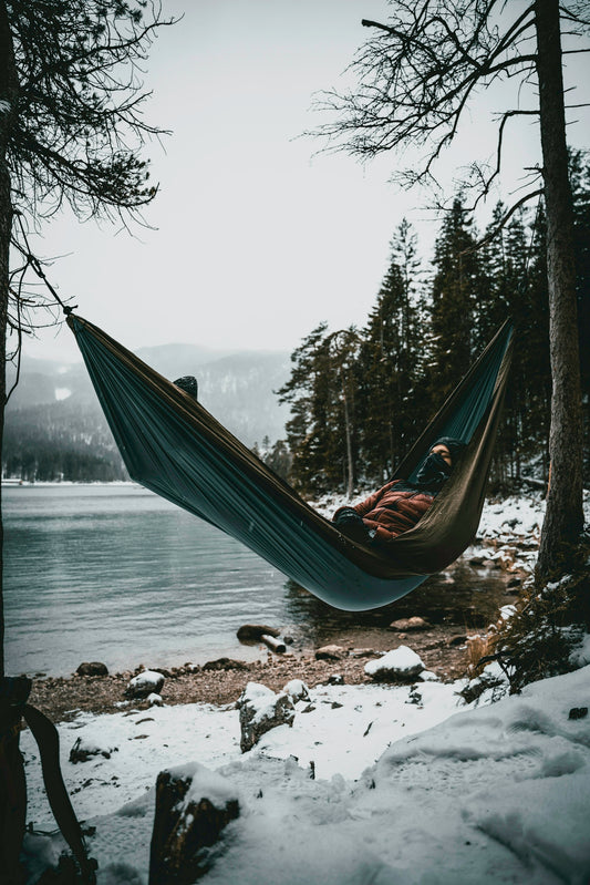 a person laying in a hammock by a lake