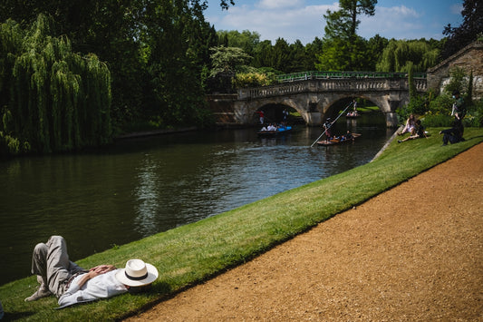 a person lying on the grass next to a river with a bridge